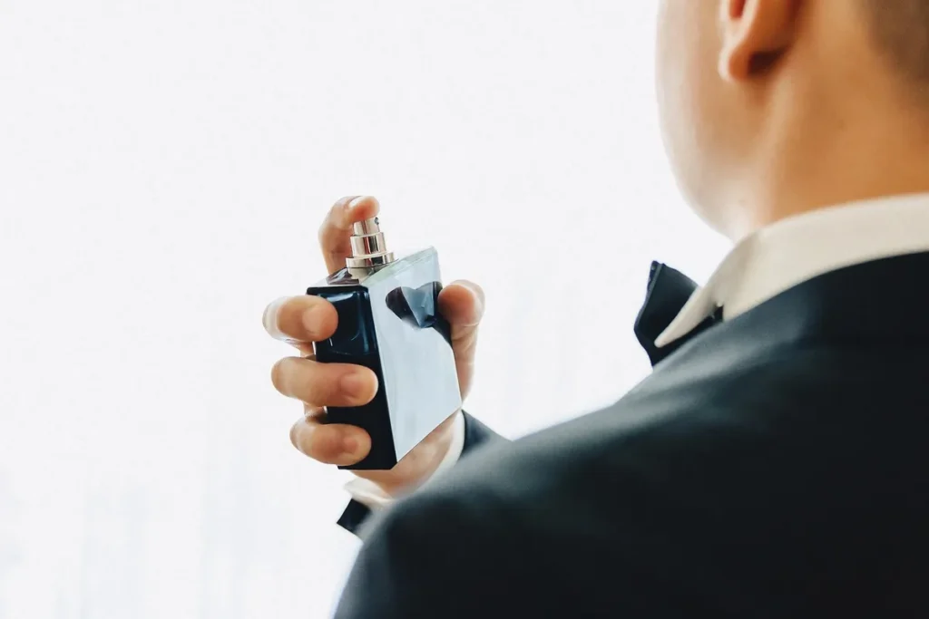 Homem de terno borrifando perfume no pescoço antes de um evento formal.
