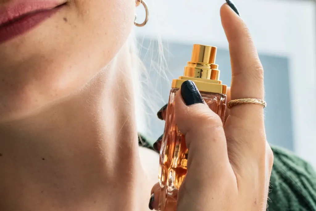 Mulher aplicando perfume no pescoço com frasco elegante de vidro e tampa dourada.