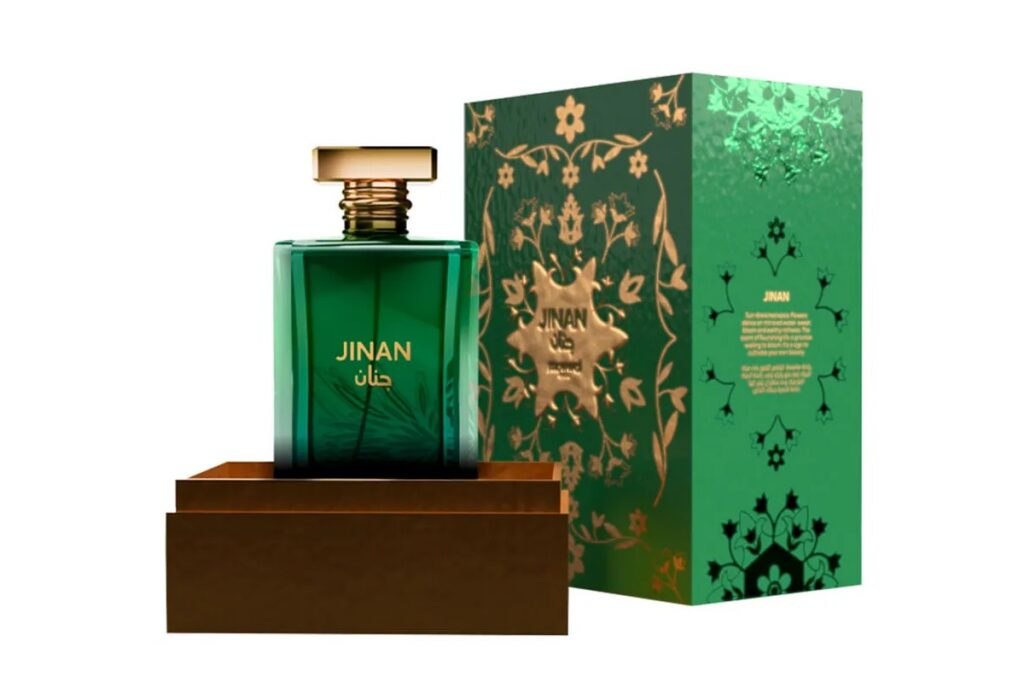 Perfume Jinan em frasco verde com tampa dourada, exibido sobre base marrom ao lado de caixa verde decorada com arabescos dourados.