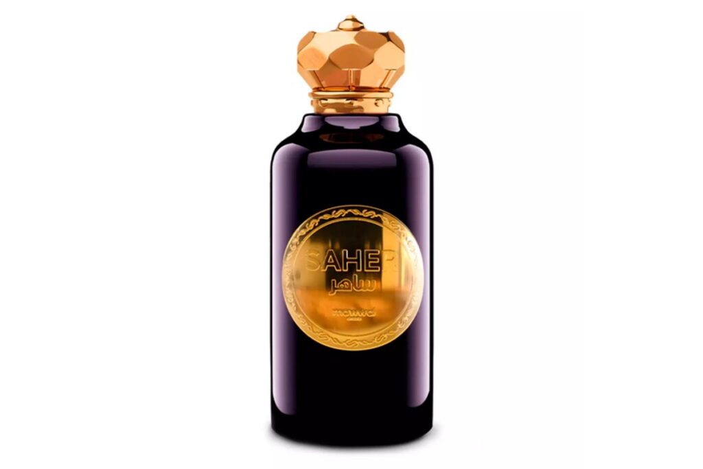 Frasco do perfume Saher na cor roxa com tampa dourada facetada e rótulo circular dourado ao centro.