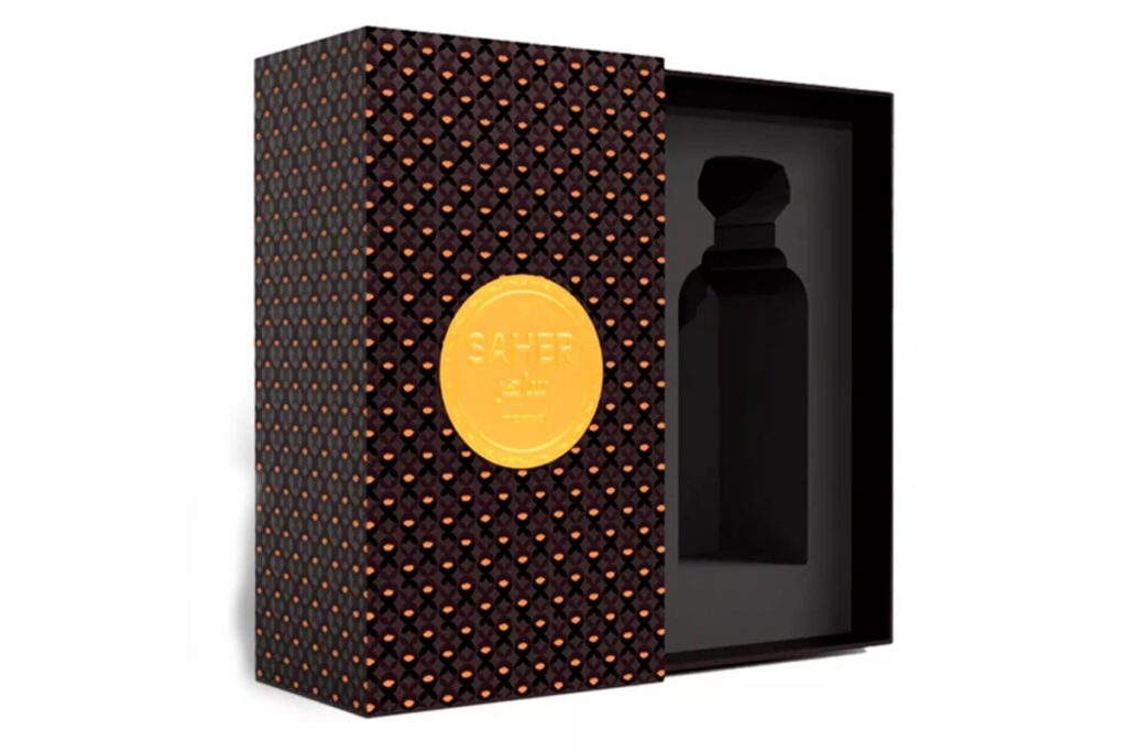 Caixa do perfume Saher parcialmente aberta, com padrão preto e dourado, medalhão frontal dourado e interior moldado para acomodar o frasco.