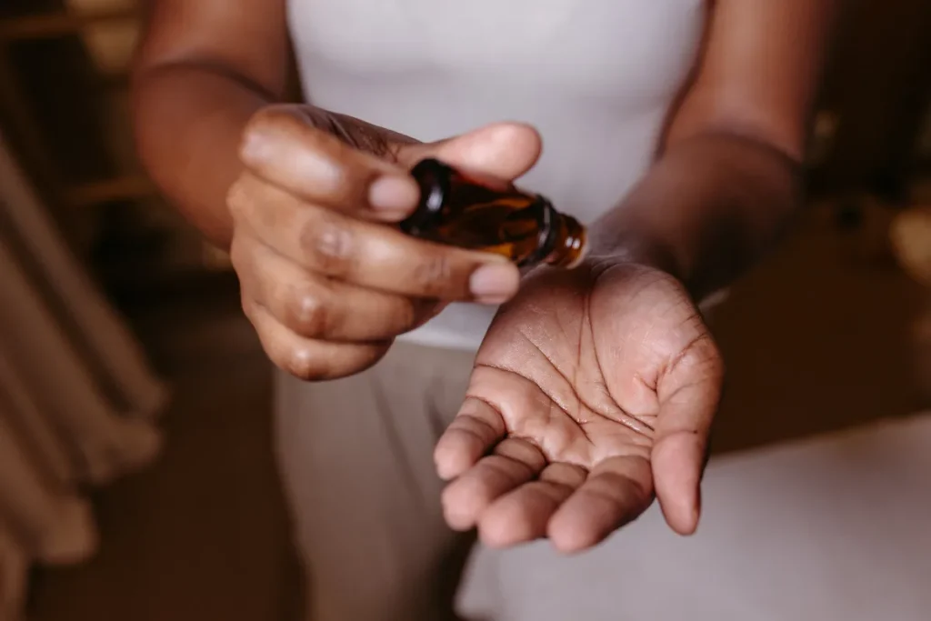 mãos segurando um pequeno frasco de óleo enquanto o líquido é aplicado na palma da mão