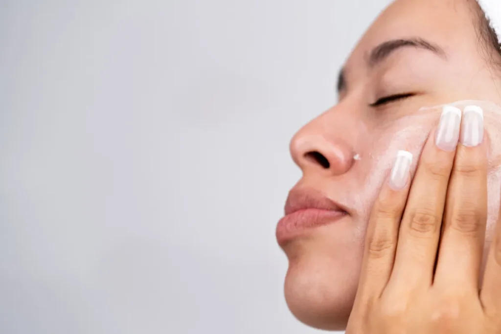 mulher espalhando creme hidratante na bochecha com a mão