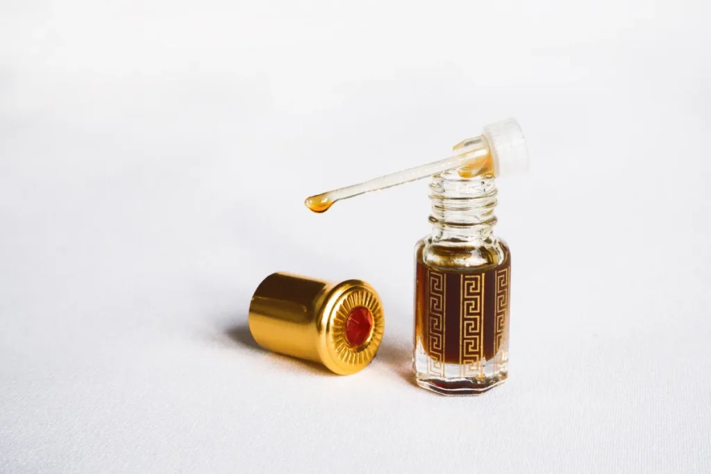 frasco pequeno de perfume com conta-gotas e líquido dourado ao lado da tampa