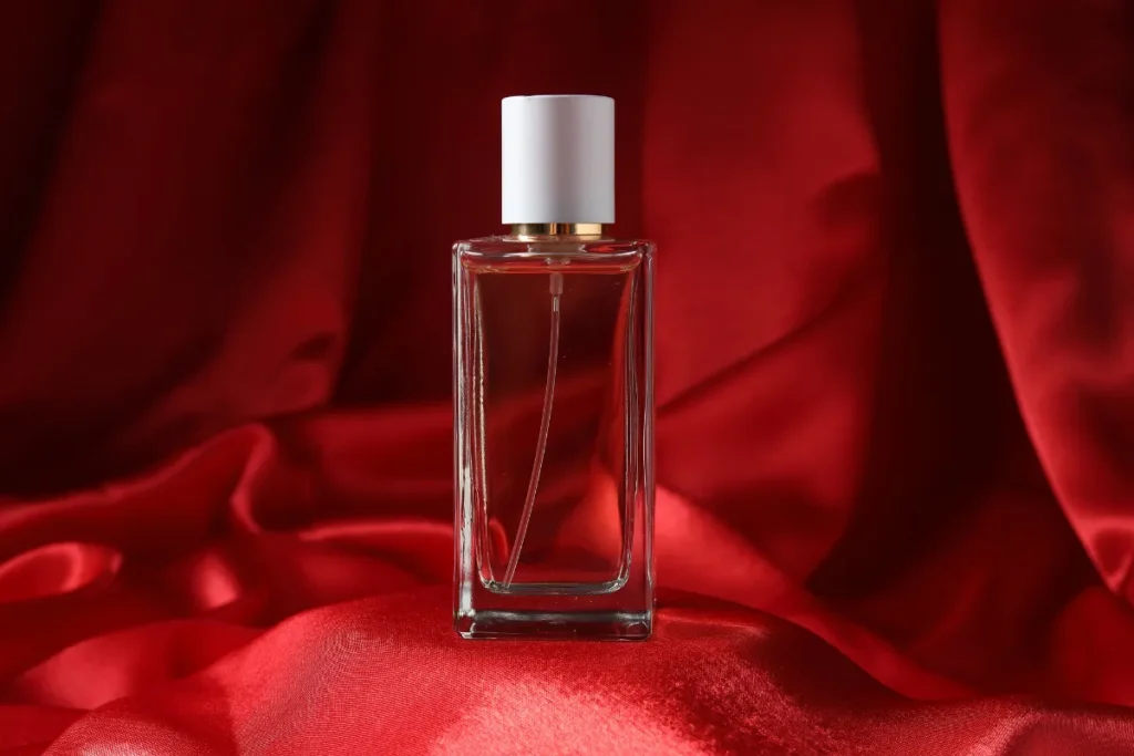 frasco de perfume transparente com líquido avermelhado colocado sobre tecido vermelho