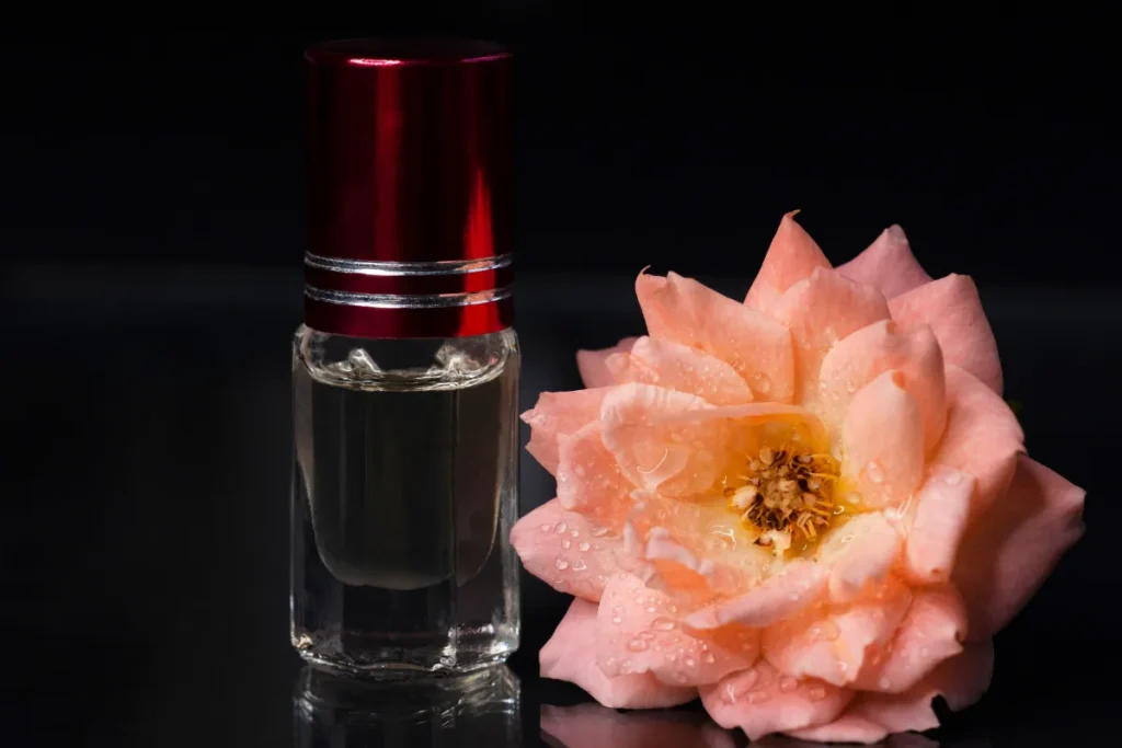 frasco pequeno de perfume com tampa vermelha posicionado ao lado de uma flor rosada