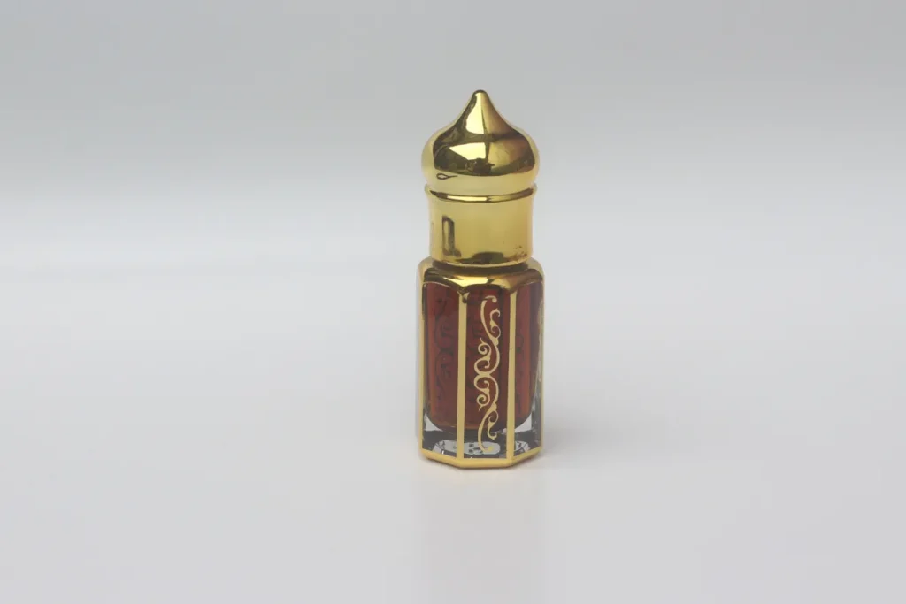 frasco pequeno de perfume árabe com tampa dourada e líquido escuro no interior