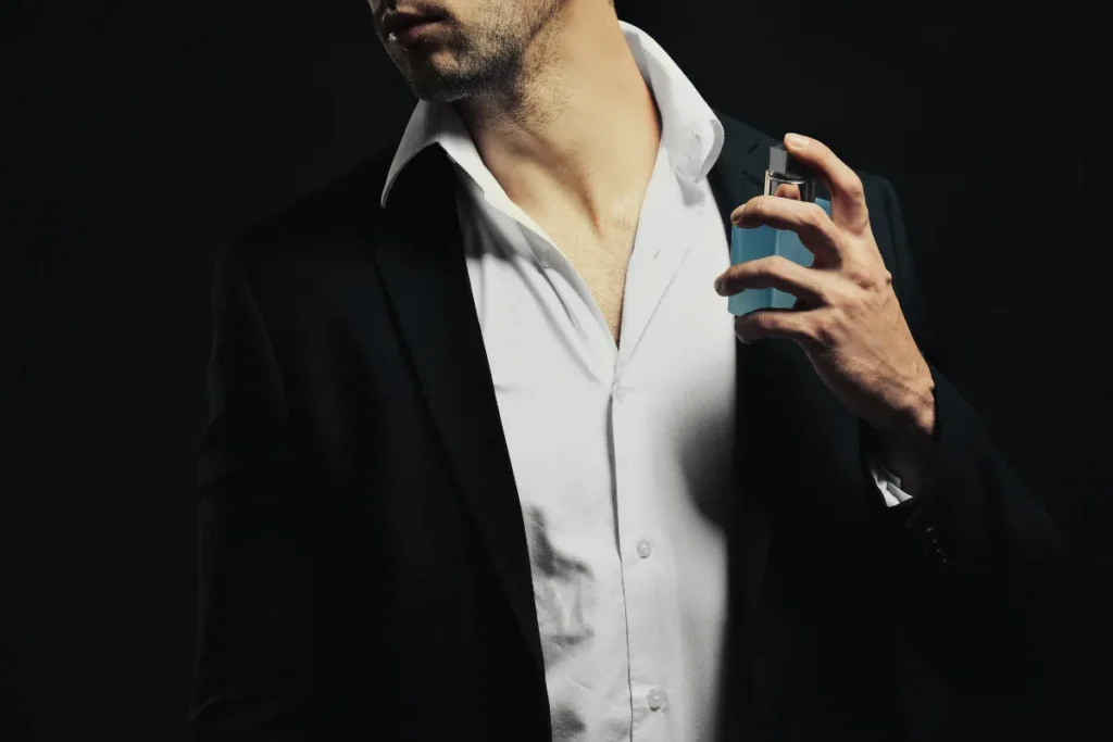 homem usando camisa branca e blazer borrifando perfume próximo ao pescoço