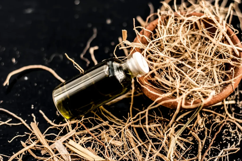 frasco pequeno de óleo escuro ao lado de raízes secas de vetiver em um recipiente