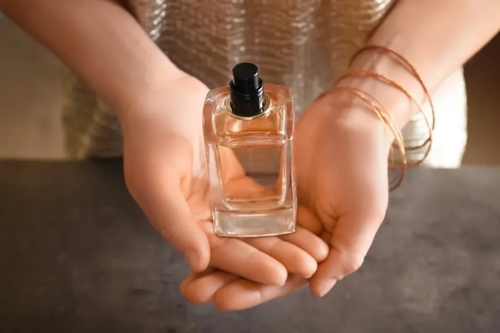 frasco de perfume feminino apoiado nas mãos com líquido rosado no interior