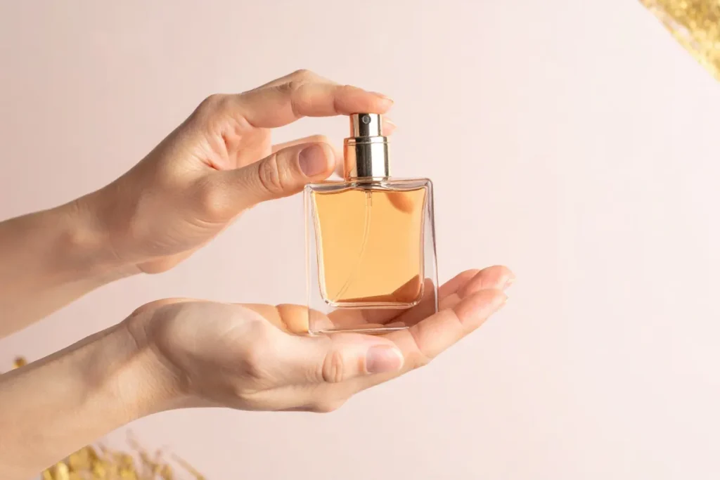 mãos segurando um frasco de perfume feminino transparente com líquido âmbar