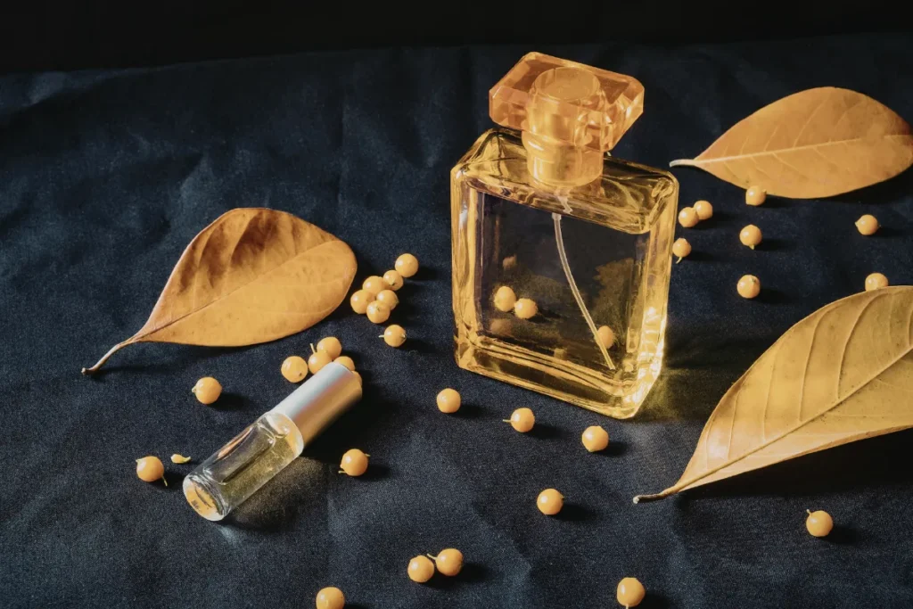 frasco de perfume transparente sobre tecido escuro cercado por folhas secas e pequenas esferas decorativas