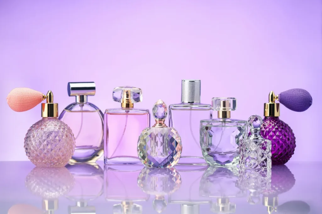 conjunto de frascos de perfume em vidro decorado com tons lilás e detalhes elegantes alinhados sobre superfície refletiva