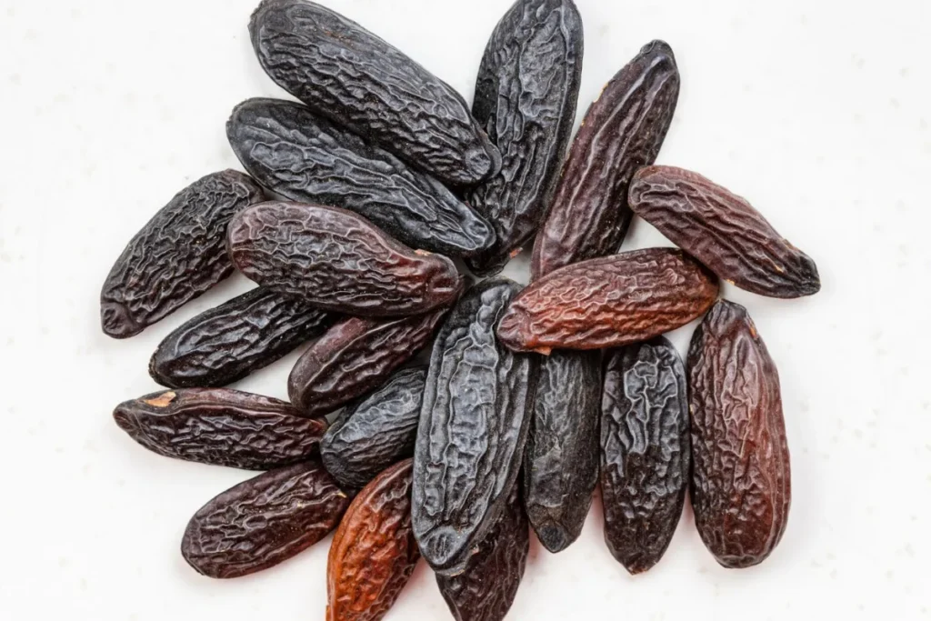 Sementes de fava tonka secas agrupadas sobre fundo claro, com textura enrugada e tonalidade marrom-escura.