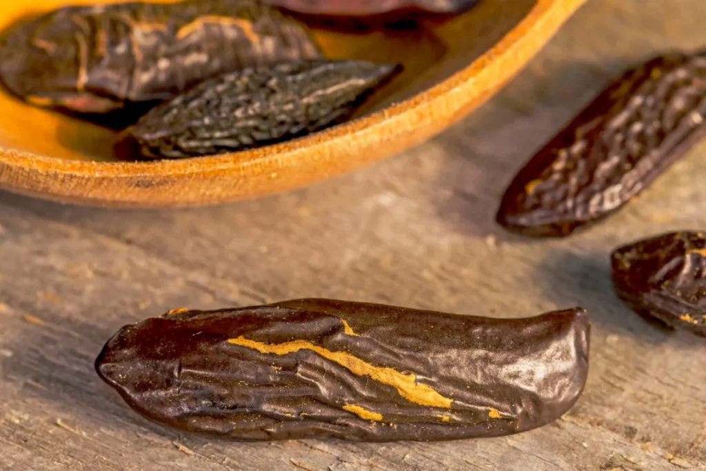 Sementes de fava tonka secas sobre superfície de madeira, com recipiente ao fundo.