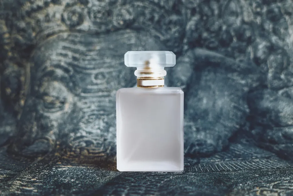 Frasco de perfume de vidro fosco com tampa transparente posicionado sobre superfície com textura escura decorativa.