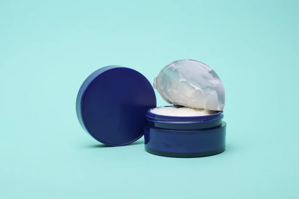 Pote azul de creme hidratante corporal aberto com a tampa ao lado sobre fundo azul claro.