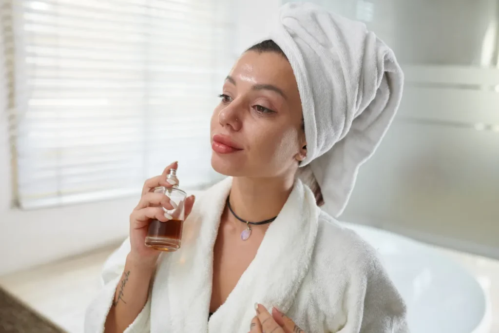 Mulher de roupão com toalha na cabeça aplicando perfume no pescoço após o banho