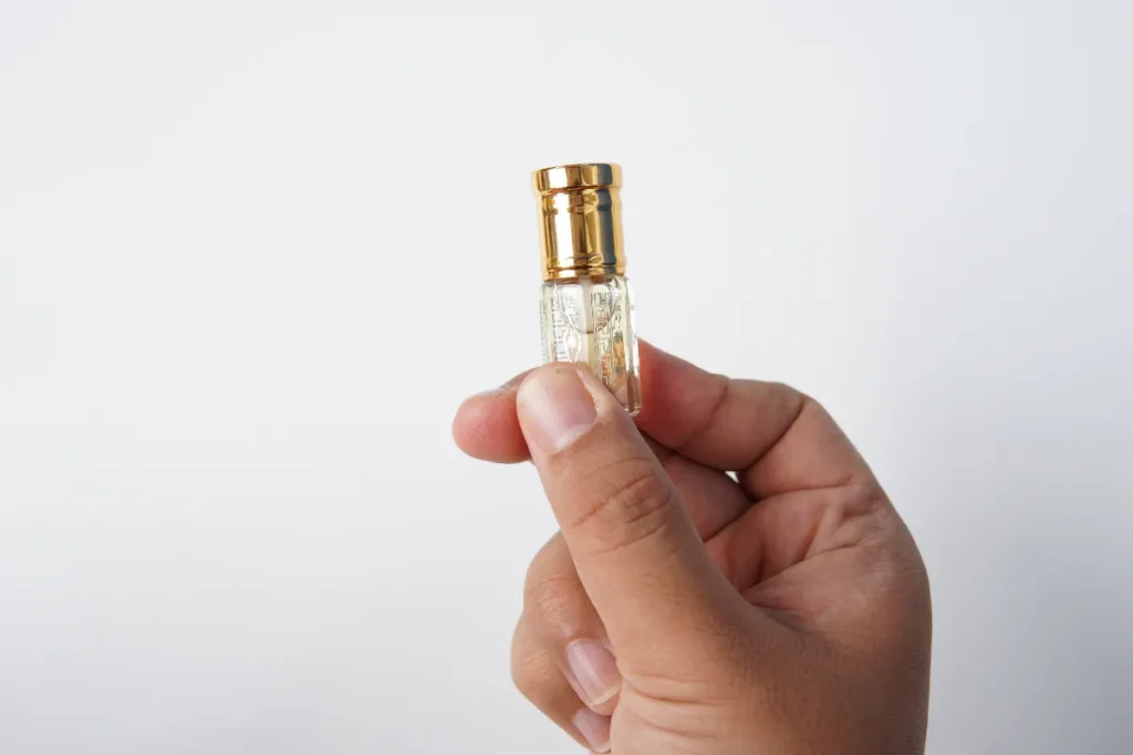 mão segurando pequeno frasco de perfume com tampa dourada em fundo neutro