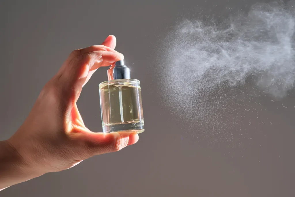 mão segurando pequeno frasco de perfume enquanto borrifa o líquido no ar