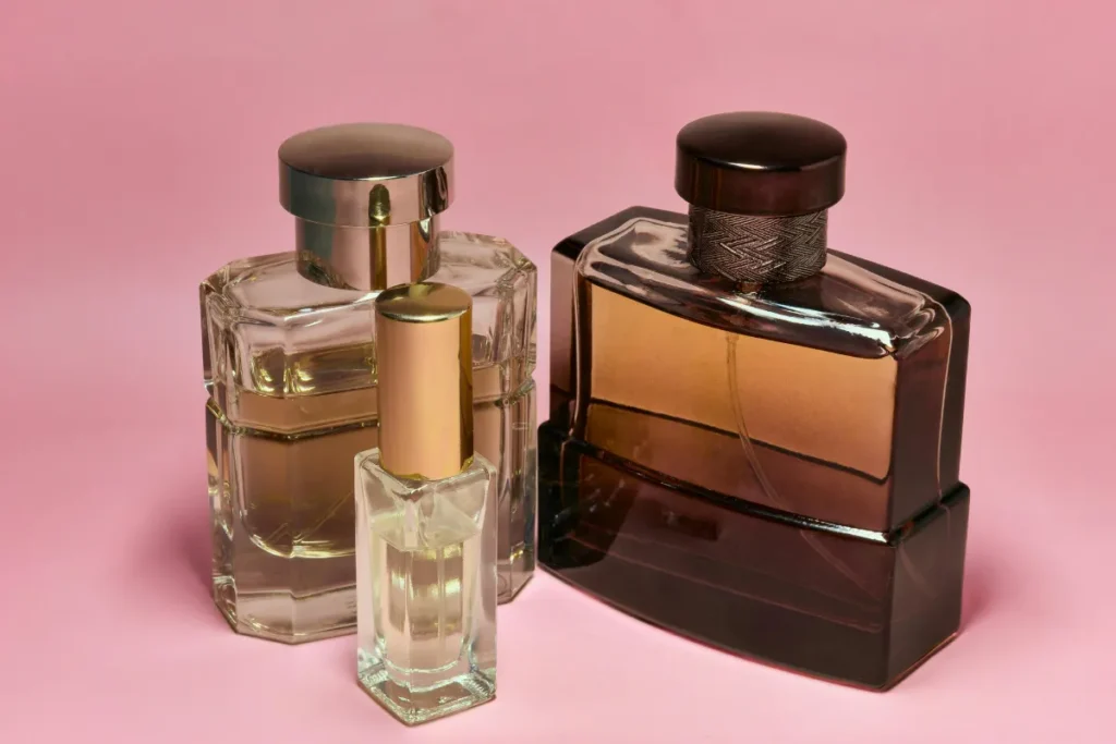 três frascos de perfume de vidro com designs diferentes posicionados sobre fundo rosa