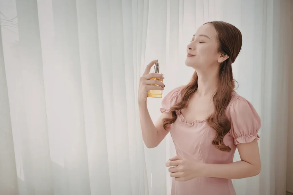 Mulher de olhos fechados borrifando perfume enquanto sente o aroma da fragrância.