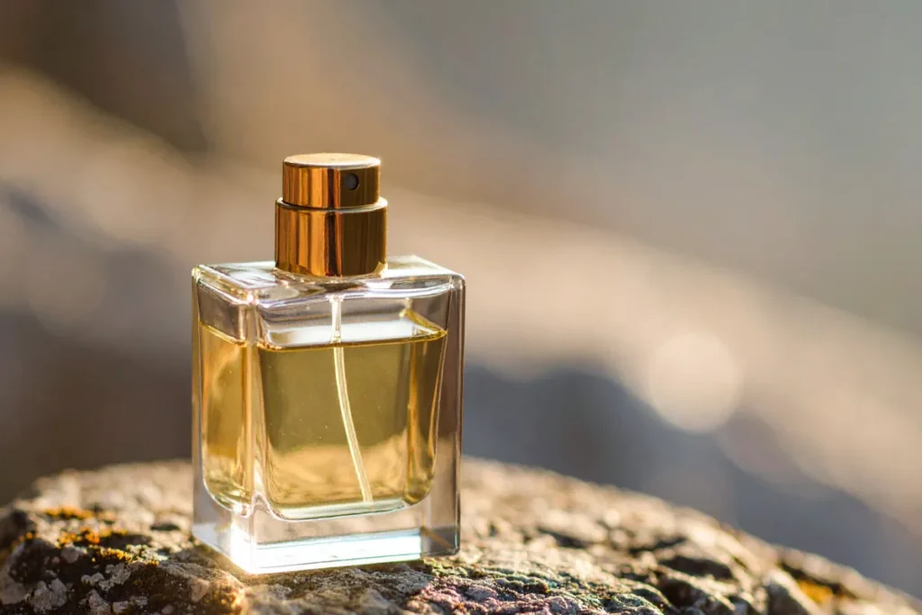 Frasco de perfume feminino com líquido dourado apoiado sobre pedra em ambiente externo