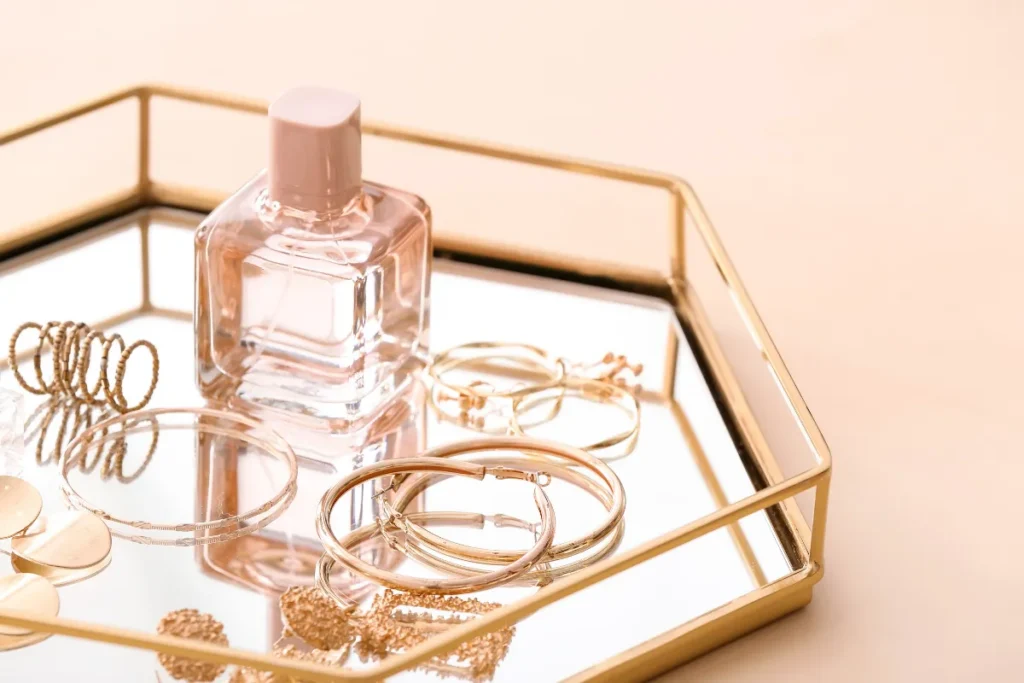 Frasco de perfume feminino transparente sobre bandeja com joias douradas em fundo claro