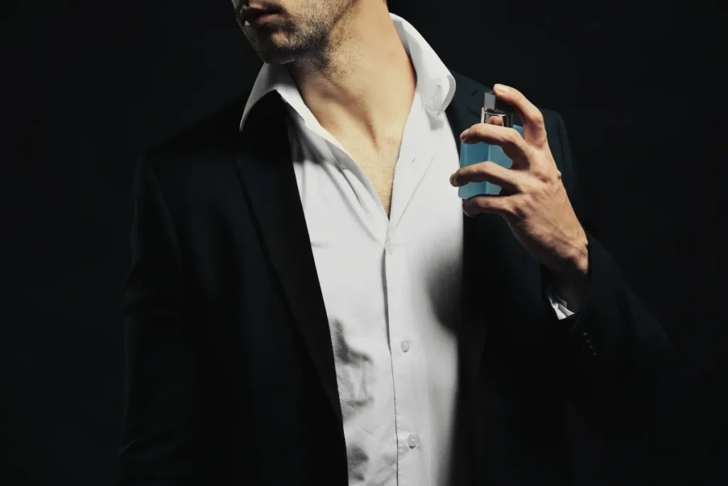 Homem de terno borrifando perfume no pescoço em fundo escuro