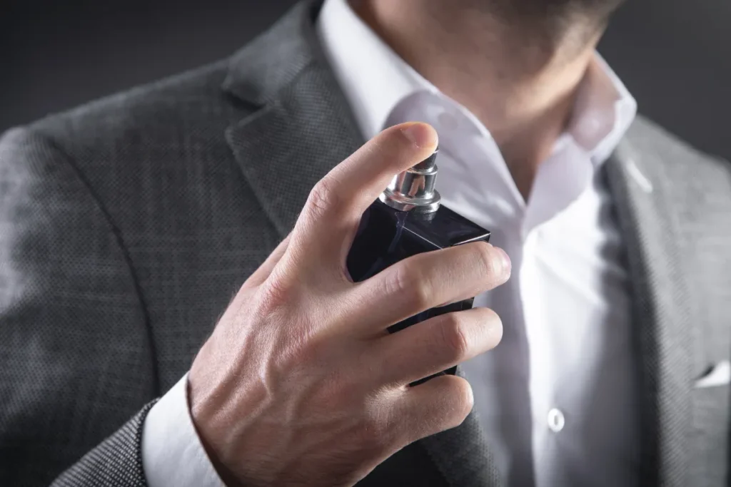 Homem segurando frasco de perfume próximo ao pescoço prestes a aplicar