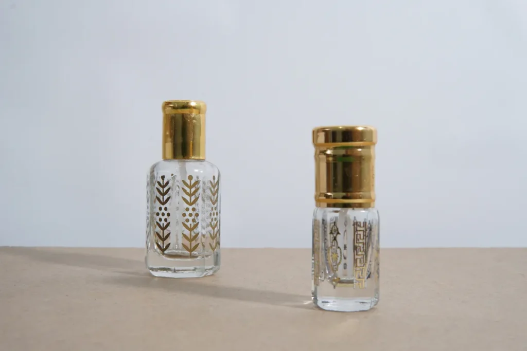 Dois frascos pequenos de perfume com detalhes dourados sobre superfície clara.