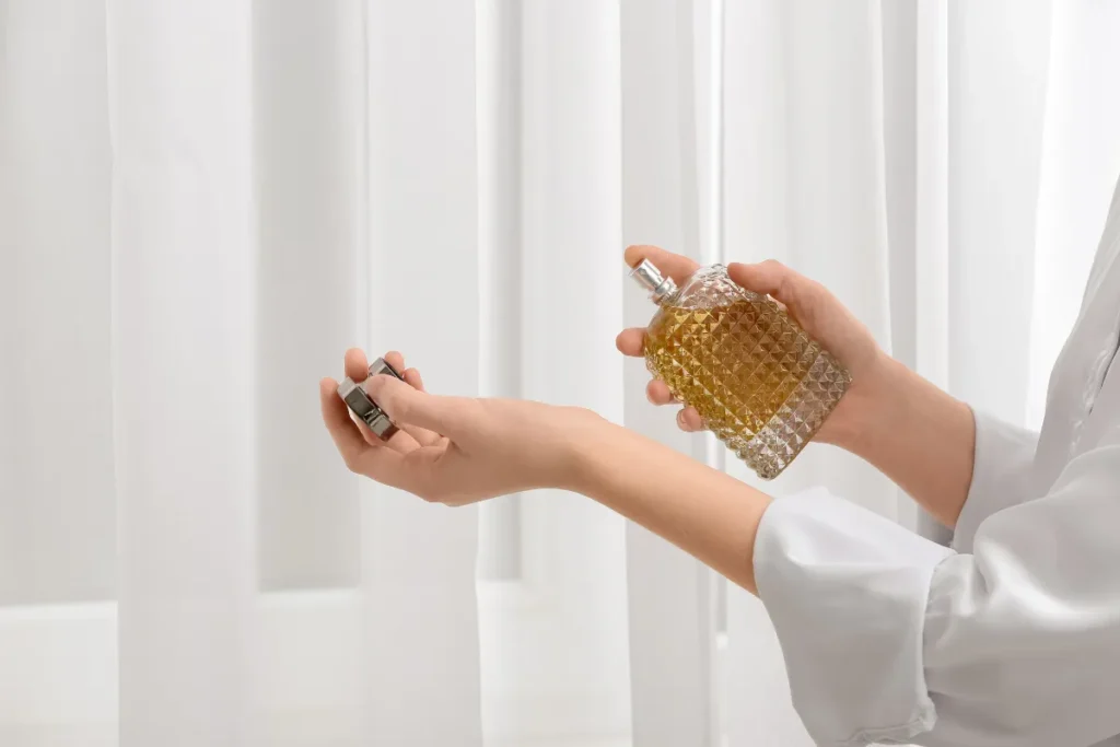 Pessoa borrifando perfume de frasco dourado com textura geométrica sobre o pulso.