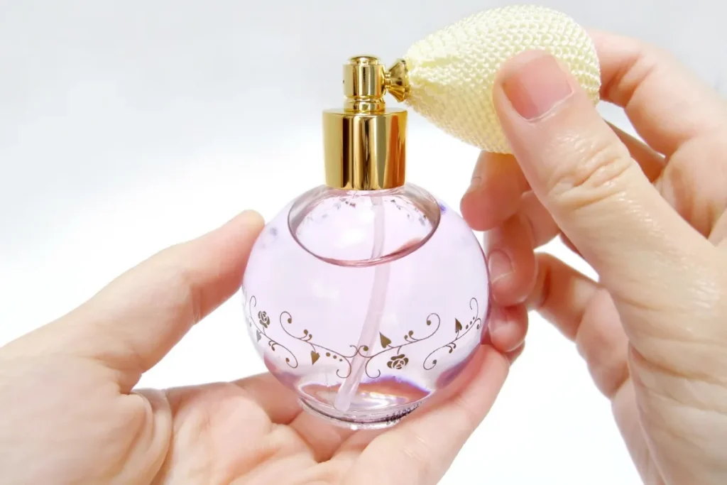 Mãos segurando frasco de perfume com aplicador tipo bulbo pressionável