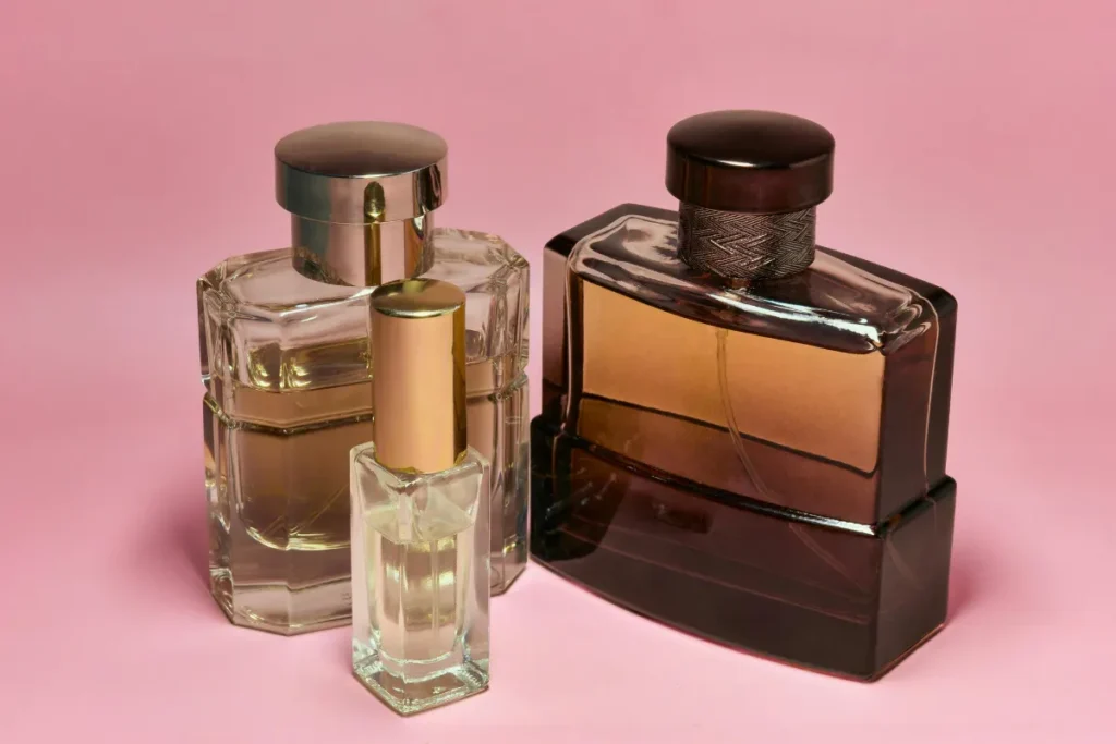 Três frascos de perfume com design elegante em vidro transparente e âmbar sobre fundo rosa.