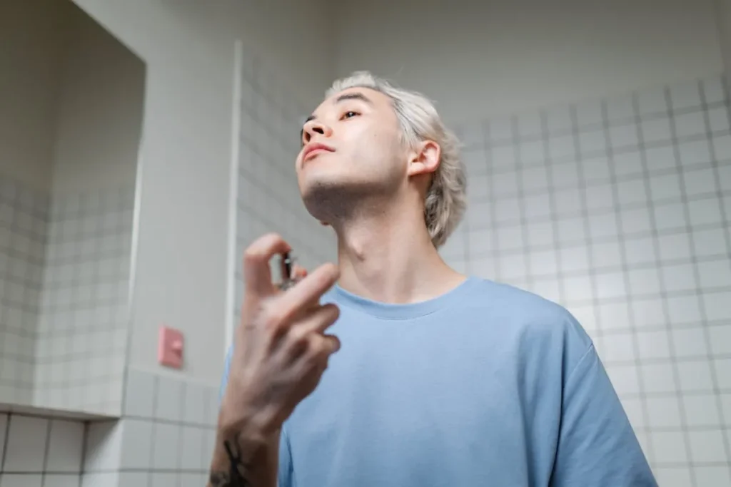 homem aplicando perfume no pescoço em ambiente interno após se arrumar