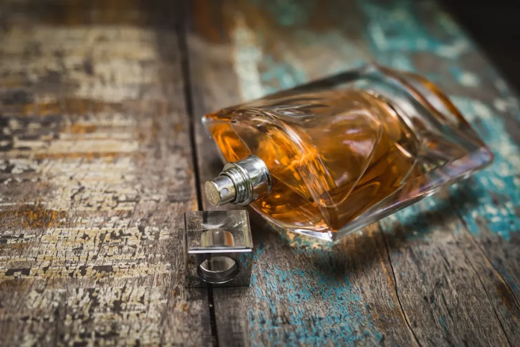 frasco de perfume com líquido ambar deitado sobre superfície de madeira com tampa ao lado